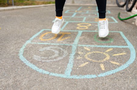 Photo for Close-up of a girl's feet and hopscotch painted on the asphalt. A child plays hopscotch on an outdoor playground on a sunny day. outdoor activities for children. - Royalty Free Image