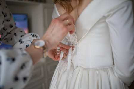 Téléchargez les photos : Jour du mariage. Aider la mariée à mettre sa robe de mariée. - en image libre de droit