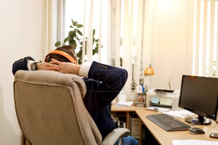 Téléchargez les photos : Heureux jeune homme d'affaires avec écouteurs ayant pause dans le bureau moderne - en image libre de droit