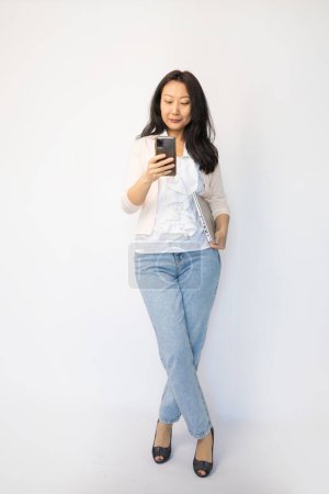 Asiatische Geschäftsfrau schreibt jemandem eine SMS, isoliert vor weißem Hintergrund.