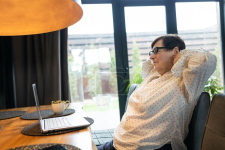 Müde gestresste ältere Geschäftsfrau, die unter Nackenschmerzen leidet, wenn sie vom Homeoffice aus am Tisch sitzt. Frau macht ein Nickerchen und entspannt sich mit nach hinten geneigtem Kopf.