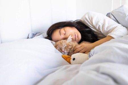 Joven mujer asiática con lindo gato durmiendo en cama
