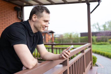 Ein junger Mann mit einem Handy auf der Terrasse eines Hauses