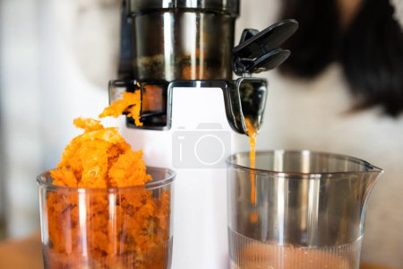 Asian woman making freshly juice from carrots and apple. Operation of the juicer. 