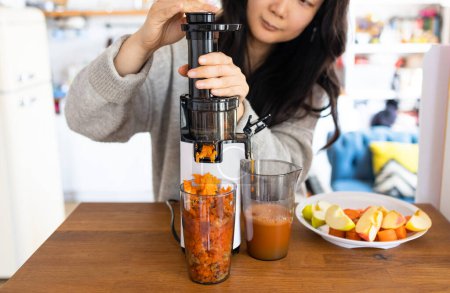 Mujer asiática haciendo jugo fresco de zanahorias y manzana. Funcionamiento del exprimidor. 