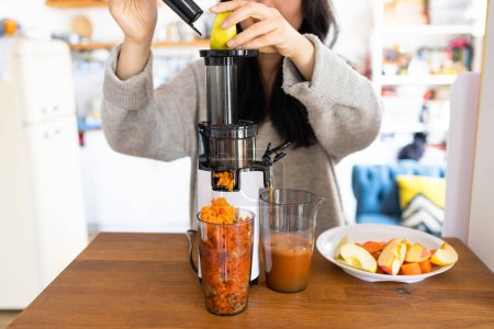 Mujer asiática haciendo jugo fresco de zanahorias y manzana. Funcionamiento del exprimidor. 