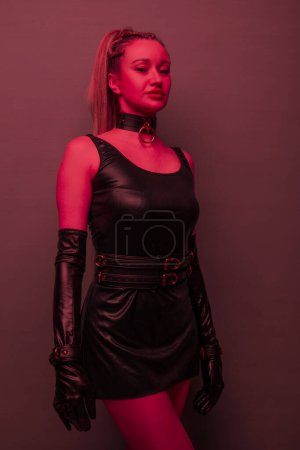 Foto de Beautiful young woman in a leather dress and bondage set posing on red light backgound - Imagen libre de derechos