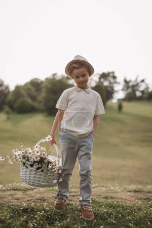 Téléchargez les photos : Un beau garçon dans un chapeau avec un panier avec un bouquet de marguerites s - en image libre de droit