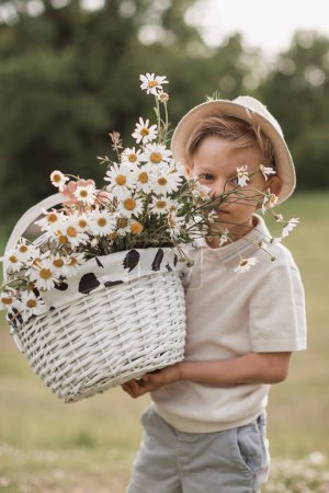 Téléchargez les photos : Mignon garçon dans la nature renifler un bouquet de marguerites de champ en paille - en image libre de droit