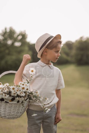 Téléchargez les photos : Un beau garçon dans un chapeau avec un panier avec un bouquet de marguerites s - en image libre de droit
