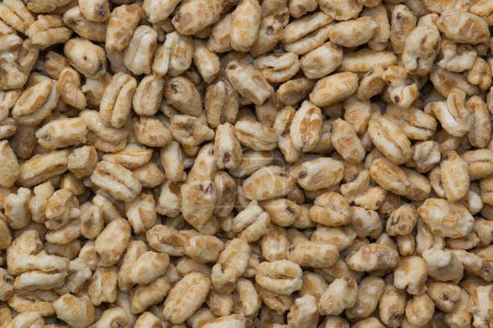 Téléchargez les photos : Dry honey puffed wheat cereal pieces scattered loosely directly above. Breakfast foods textured background, full frame image. - en image libre de droit