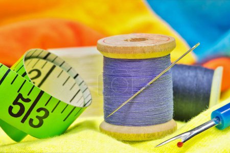 Téléchargez les photos : Outils de couture sur vêtements colorés avec des détails macro, y compris des bobines de fil, aiguille, ruban à mesurer et sélecteur de fil. - en image libre de droit