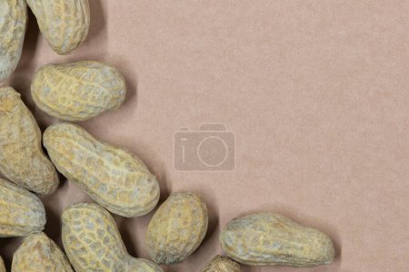 Unshelled peanuts scattered on cardstock background with copy space. Flat lay closeup food, legume crop nutrition and allergy, farming industry concept.