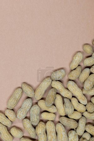 Unshelled peanuts scattered on cardstock background with copy space. Flat lay closeup food, legume crop nutrition and allergy, farming industry concept vertical format.