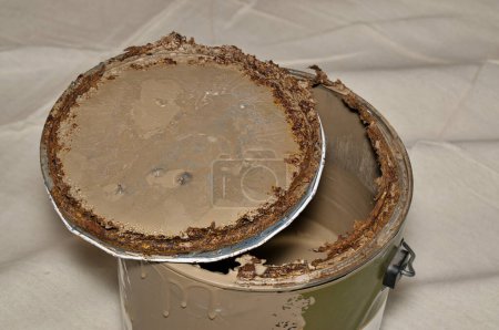 Rusted old metal paint tin with open lid on drop cloth brown expired storage concept.