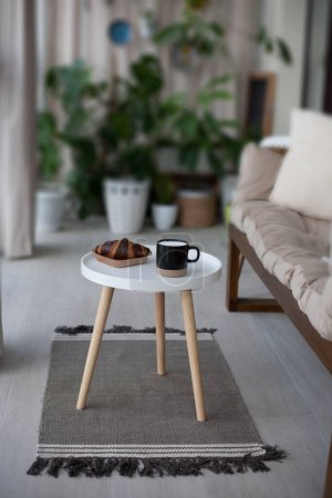 Foto de Mesa con croissant, taza y sillón suave en sala de estar ligera - Imagen libre de derechos