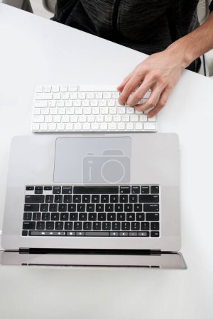 Foto de Recortado disparo de hombre escribiendo con el ordenador portátil en el lugar de trabajo en la superficie blanca para maqueta - Imagen libre de derechos