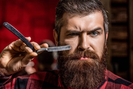 Photo for Straight razor, barbershop, beard. Vintage straight razor. Mens haircut. Man in barbershop. Handsome bearded hairdresser is holding a straight razor while barbershop. - Royalty Free Image