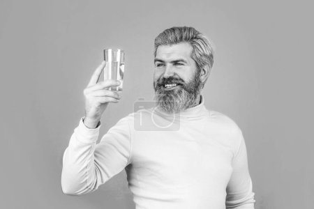 Téléchargez les photos : Heureux homme barbe boire de l'eau. Homme souriant tenant du verre transparent dans sa main. Noir et blanc. - en image libre de droit