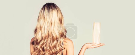 Téléchargez les photos : Femme tenant une bouteille de shampooing. Belle fille blonde avec une bouteille de shampooings dans les mains. Fille aux cheveux brillants et longs. - en image libre de droit