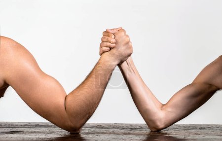 Heavily muscled man arm wrestling a puny weak man. Two mans hands clasped arm wrestling, strong and weak, unequal match.