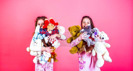 Photo for Girls holds heap of teddy bears. Girl hugging teddybears, childhood. Two beautiful happy girls standing and embracing plushs toy in children room. Joy and smile concept. - Royalty Free Image