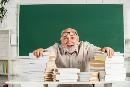 Photo for Portrait male teacher in classroom. Funny teacher hold many books at school. Teacher with books in school. Man elementary school teacher standing in classroom. Old man teachers on green board. - Royalty Free Image