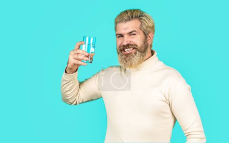 Téléchargez les photos : Homme souriant tenant du verre transparent dans sa main d'eau. Un homme buvant dans un verre d'eau. Soins de santé concept photo, mode de vie. Homme barbe heureux eau potable. - en image libre de droit