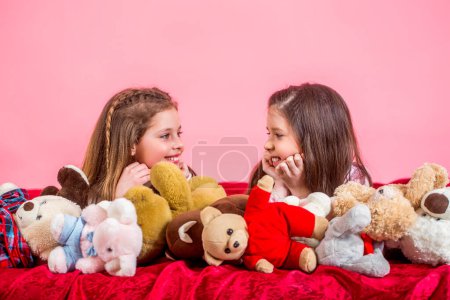 Photo for Girl sisters in pajamas lie in bed. Pajama party. Homewear for kids. Children in soft warm pajamas playing home. Girls in colorful pajamas hold funny stuffed animals, childhood, happiness. - Royalty Free Image