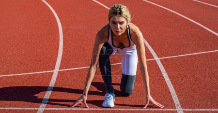 Woman getting ready to start on stadium. Women sprinters at starting position ready for race on racetrack. Girl getting ready at starting position line for sprint.