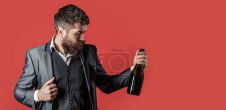 Mann hält Flasche mit Champagner und Glas über rotem Hintergrund. Die Person hält eine Rotweinflasche in der Hand. Mann hält Flasche mit Champagner, Wein. Kopierraum.