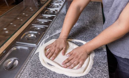 Chef preparando las manos de masa de pizza. Masa de pizza enrollada y amasada. Cocine las manos amasando la masa, espolvoreando un trozo de masa con harina de trigo blanco. Las manos amasan la masa para hacer pizza.