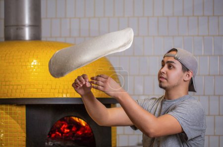 Skilled chef preparing dough for pizza rolling with hands and throwing up. The chef tosses the pizza dough into the air. Hands of a male chef with thin round pizza dough in the kitchen.