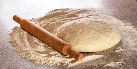 Fresh raw dough and rolling. Raw dough for pizza or bread baking. Rolled doughs with rolling pin on table covered baking flour. Wooden rolling pin with freshly prepared dough, flour shaker.