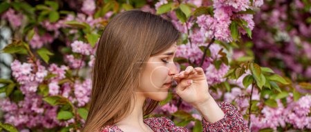 Photo for Woman sneezing into a handkerchief near a tree full of blossoms. She is suffering from seasonal spring allergy. Pollen allergy, girl sneezing. Woman sneezing in front of blooming tree. - Royalty Free Image