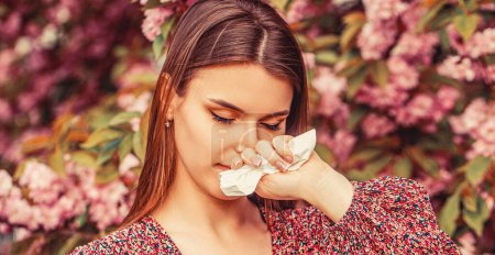 Photo for Woman wiping her nose.Woman sneezing into a handkerchief near a tree full of blossoms. She is suffering from seasonal spring allergy. - Royalty Free Image