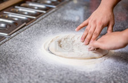 Las manos amasan la masa para hacer pizza, harina. Chef preparando las manos de masa de pizza. Masa de pizza enrollada y amasada. Cocine las manos amasando la masa, espolvoreando un trozo de masa con harina de trigo blanco.
