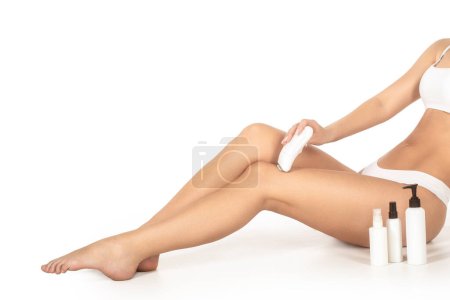 Téléchargez les photos : Épilateur électrique à jambes rasées. Femme épilte sa jambe avec un épilateur électrique dans la salle de bain. Jambe de femme épilante avec bande de cire au spa de beauté. Gros plan femme épilation jambe dans spa. - en image libre de droit
