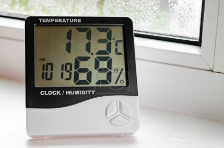 Téléchargez les photos : Un hygromètre avec thermomètre se trouve sur le rebord de la fenêtre avec condensation. Fenêtres plastiques. - en image libre de droit