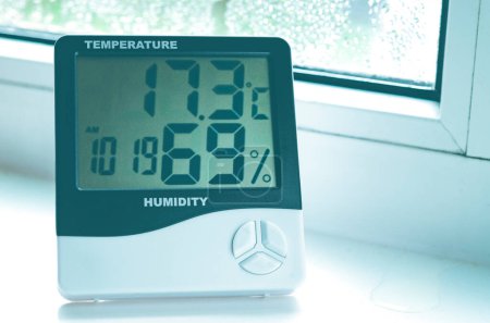 A hygrometer with a thermometer stands on the windowsill with condensation. Plastic windows.