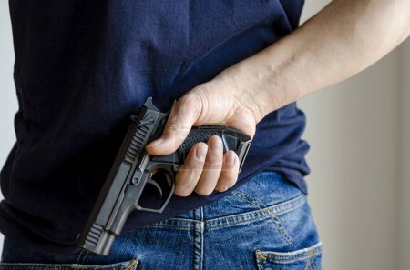 Foto de Una pistola en su mano detrás de la espalda del hombre. Armas en la mano. Armas ocultas - Imagen libre de derechos