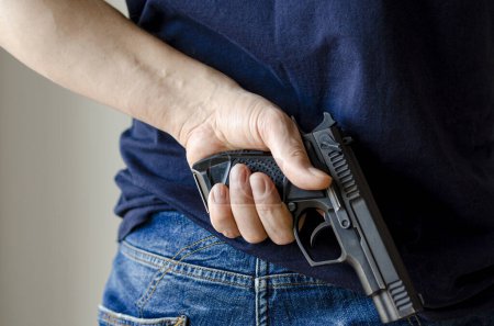 Foto de Una pistola en su mano detrás de la espalda del hombre. Armas en la mano. Armas ocultas - Imagen libre de derechos