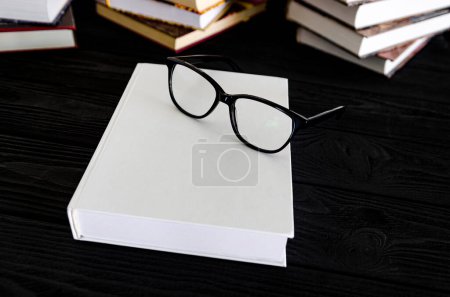 White book with space for text and black reading glasses on a black table