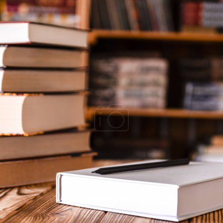 Photo for A white notebook and a black pencil on the desktop with bookshelves in the background in the library. Books - Royalty Free Image