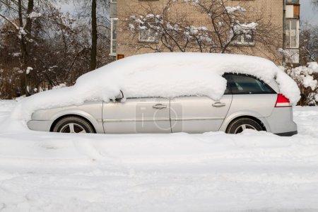 Téléchargez les photos : Voiture recouverte d'une épaisse couche de neige. Automobile après tempête de neige garée sur le côté de la rue. - en image libre de droit