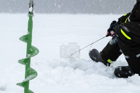 Winterangeln auf Eis. Mann wirft Köder in ein Eisloch. Entspannung in freier Wildbahn bei Schneefall.