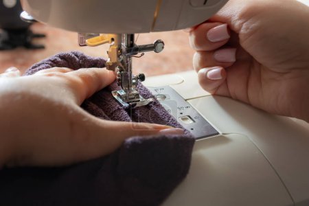 Foto de Máquina de coser con tela en hilo, prensatelas de primer plano. Manos femeninas. El proceso de coser ropa en casa. - Imagen libre de derechos