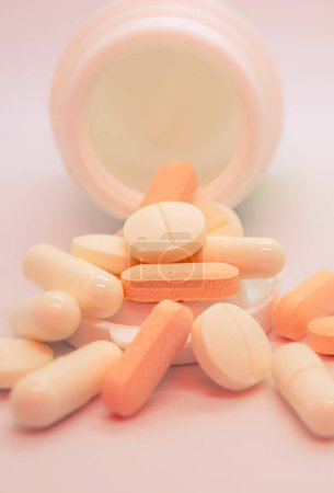 Un récipient sur le côté duquel des comprimés et des gélules de forme variée ont été distribués. Les couleurs principales des pilules sont orange, blanc crème et blanc.