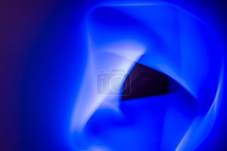 The image shows an abstract light painting with shades of blue and white. A central black shape disrupts the flow of fluid blue hues, creating a dynamic and somewhat mysterious visual effect.