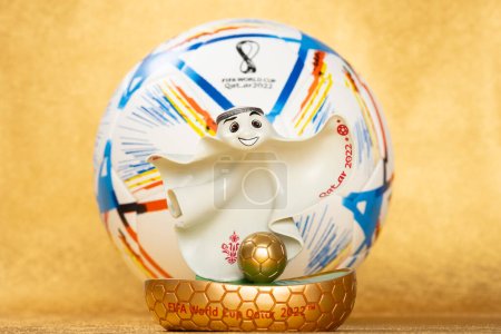 Téléchargez les photos : ZHONGSHAN Chine-Décembre 5,2022 : Qatar World Cup 2022 mascotte officielle La'eeb devant un ballon de football ou de soccer sur fond doré à composition horizontale. - en image libre de droit